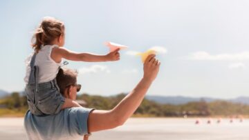 Homem com criança sobre os ombros com avião de papel na praia