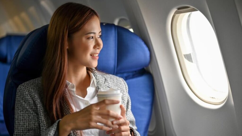 Mulher com copo de café olhando pela janela do avião