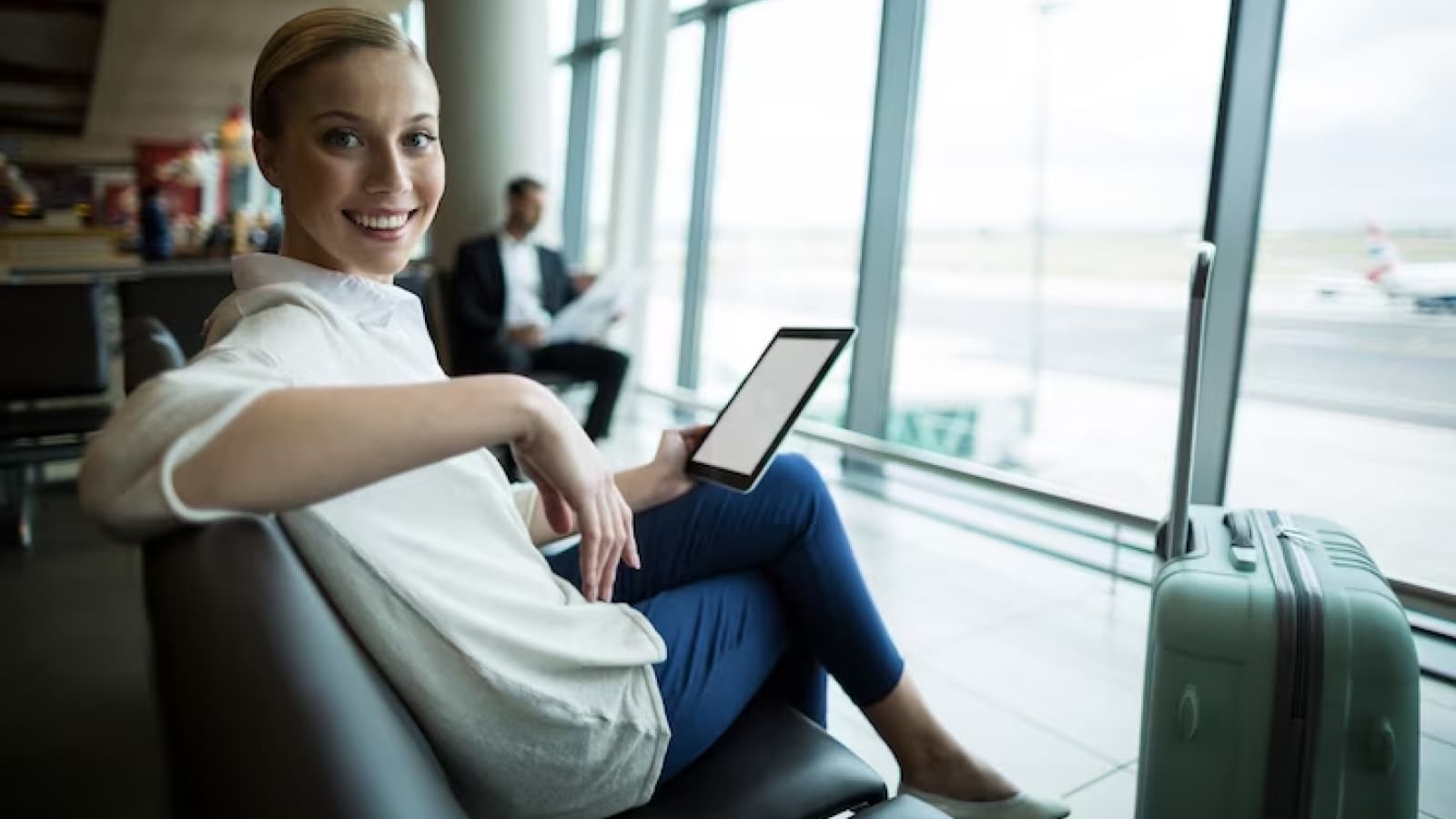 Mulher com tablet sorrindo em sala de espera de aeroporto