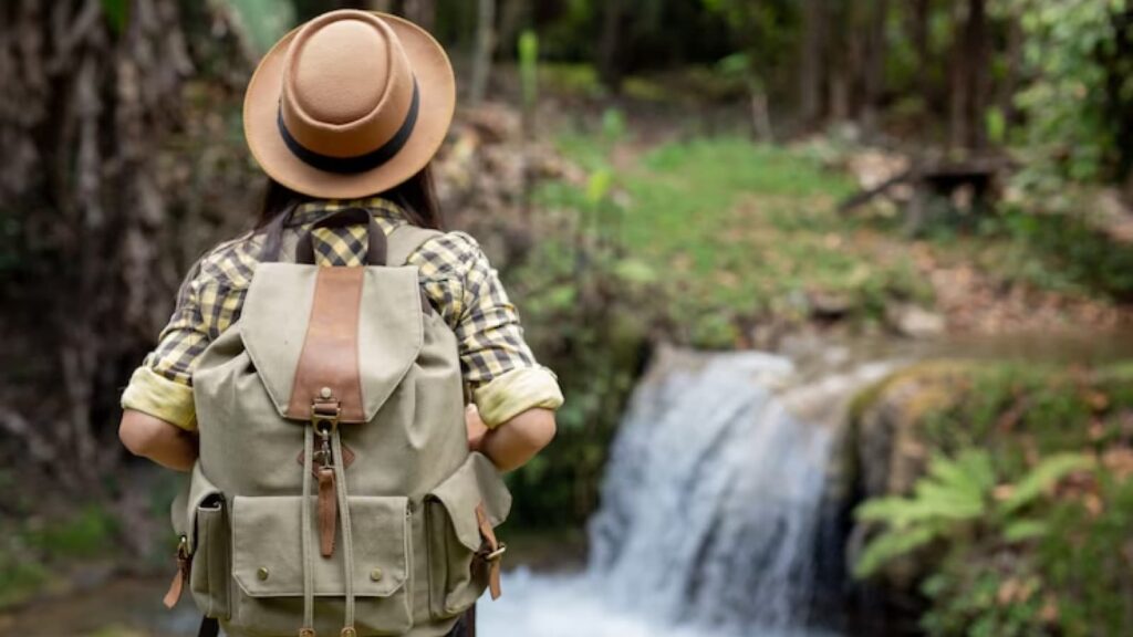 Mulher de chapéu e mochila olhando para cachoeira