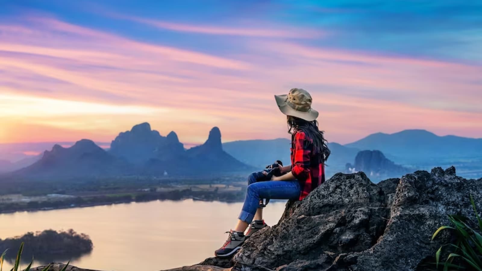 Mulher de chapéu sentada em topo de montanha