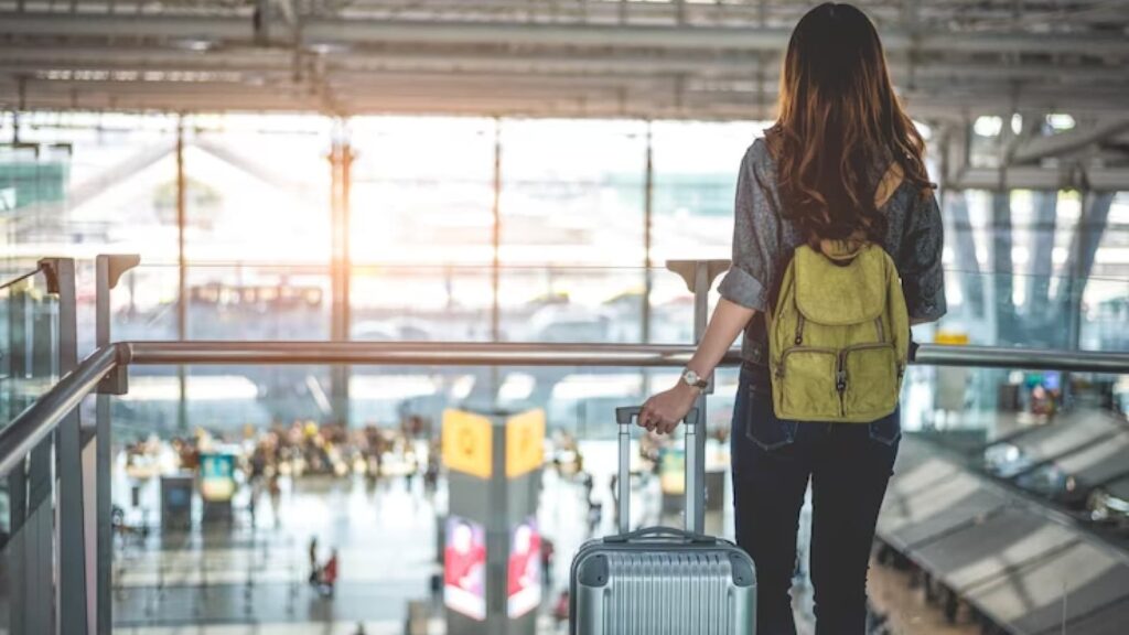 Mulher de costas com mala de viagem e mochila em aeroporto