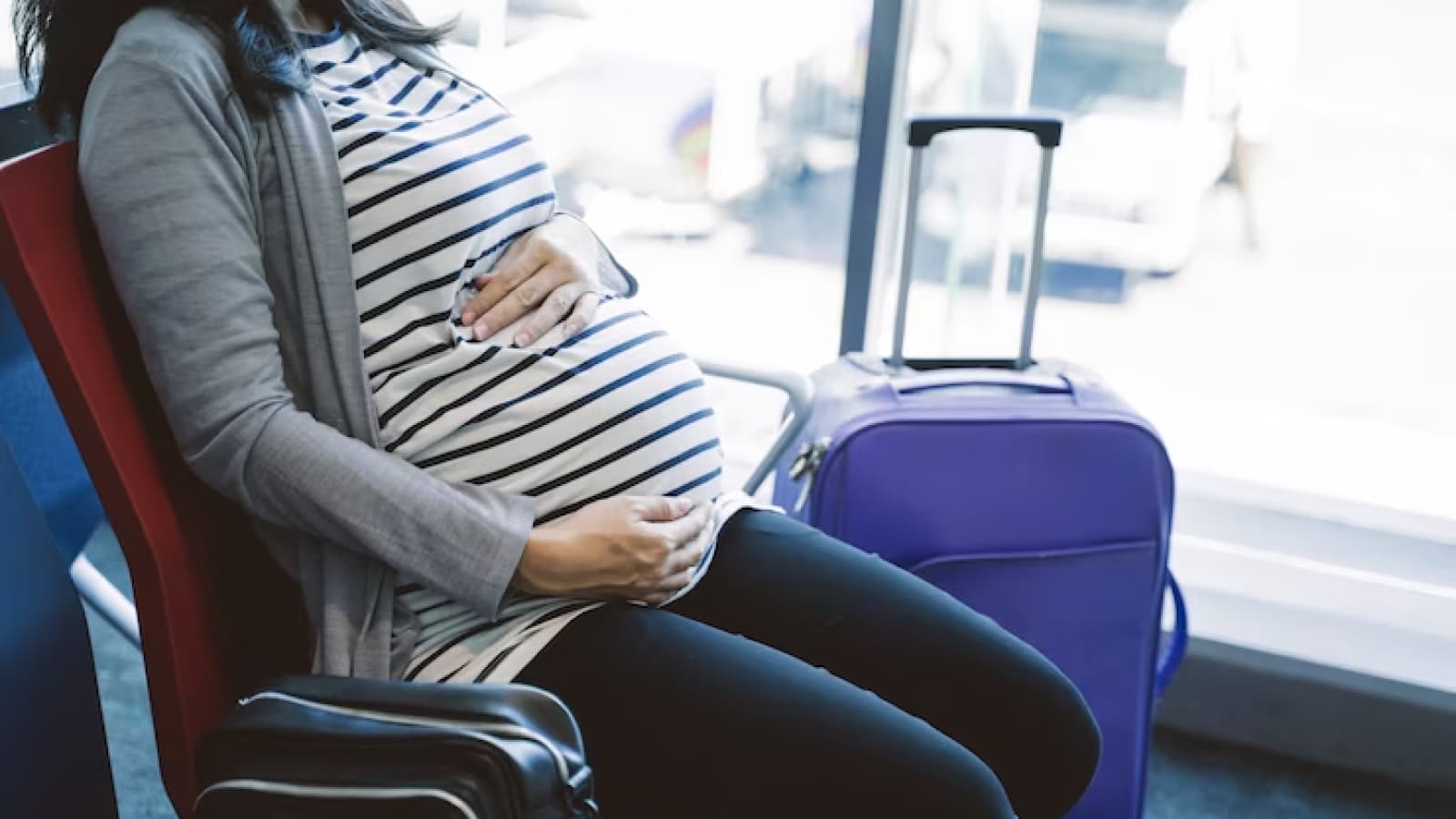 Mulher grávida em aeroporto ao lado de mala de viagem