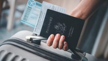 Pessoa segurando mala de viagem, passaporte e passagem